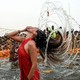 A person holds their nose while flipping their long, wet hair back after dunking in shallow water.