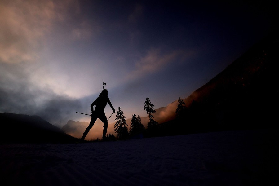 An athlete skis on a mountain path during a race, in silhouette.