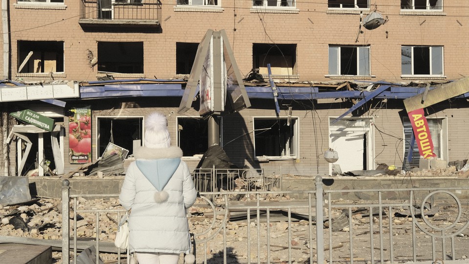 A woman in white stands before a shelled building