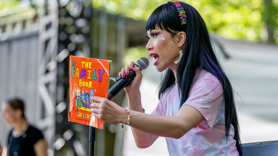 The drag queen Yuhua Hamasaki holds up "The Family Book" on an outdoor stage holding a microphone.