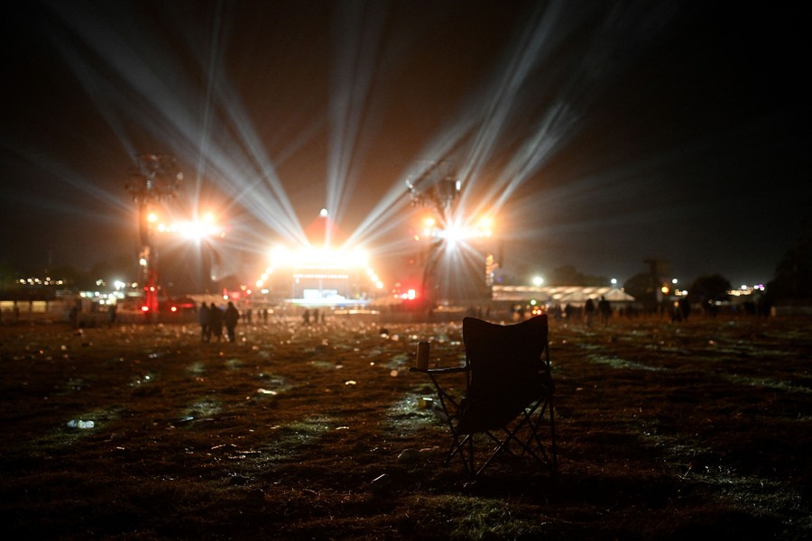 A camping chair sits discarded among other debris and a trampled field in front of an empty stage.