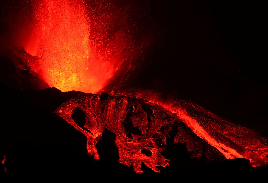 Lava erupts and flows from the top of a volcano.