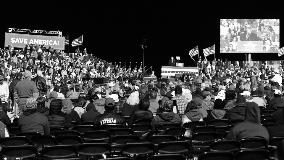 A black-and-white photo of Donald Trump speaking from a stage at a Georgia rally, taken from the perspective of a seated member of the audience.