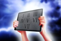 Against a stormy sky, hands hold up an iPad tablet with Roman numerals engraved on it.