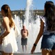 Women look on as a man stands in a fountain to cool off on a hot summer day.