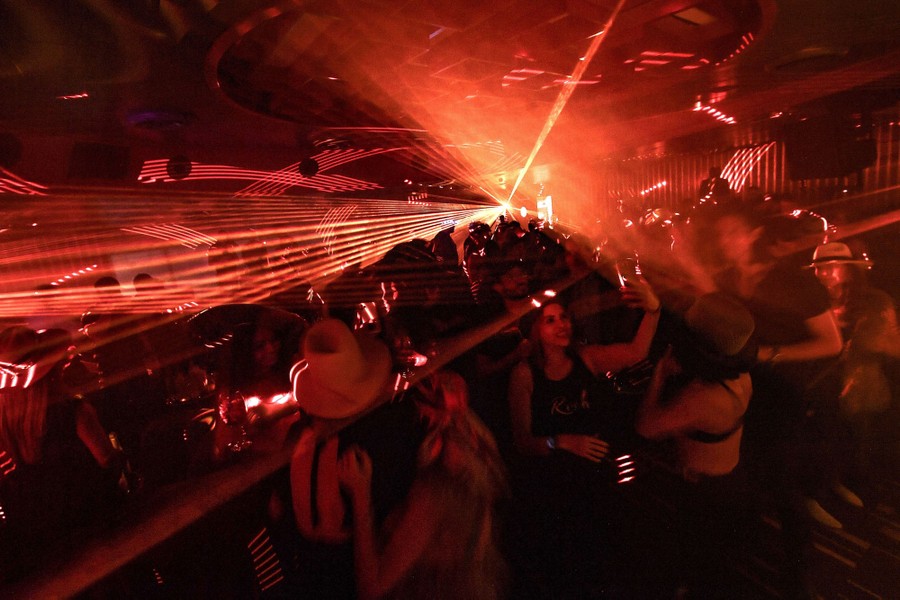 People dance in a club, surrounded by rays of flashing lights.