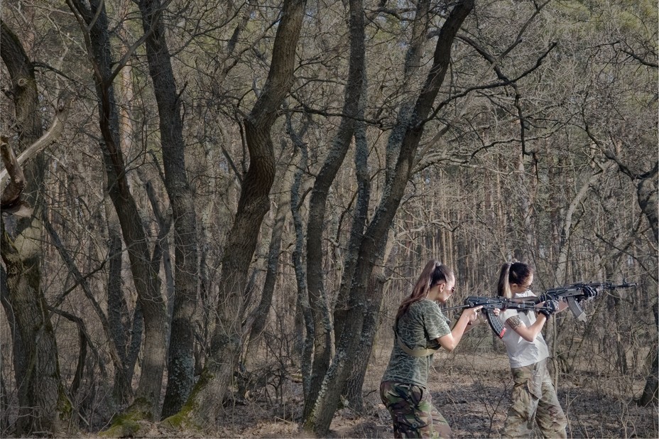 two women aim their guns in the woods