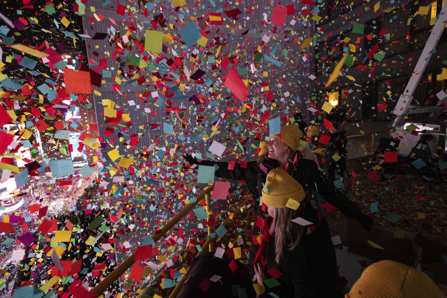People stand on a balcony, surrounded by multicolored pieces of confetti.