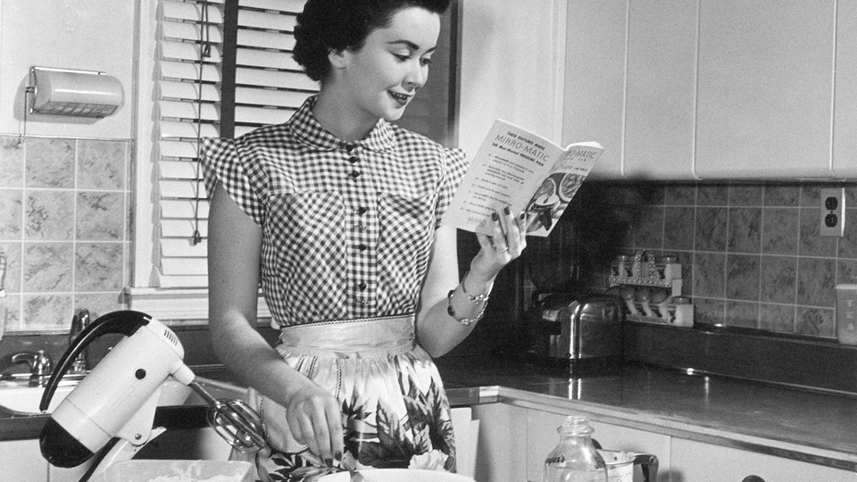 A woman reads a cookbook next to a mixer.