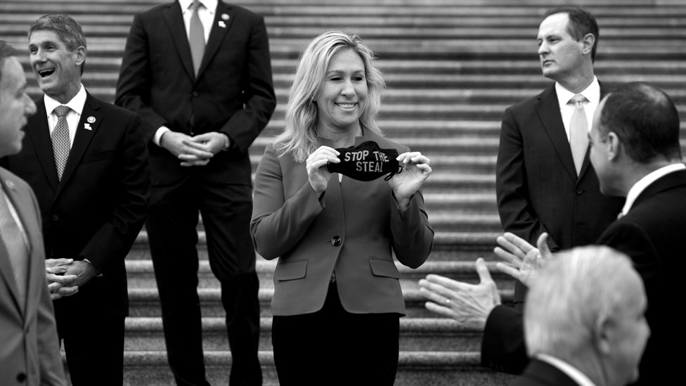Representative Marjorie Taylor Greene smiles while holding a black face mask that reads "Stop the Steal."