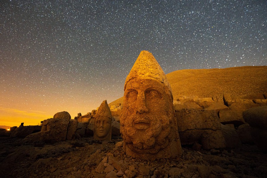 Large stone heads are seen at an archaeological site under the stars.