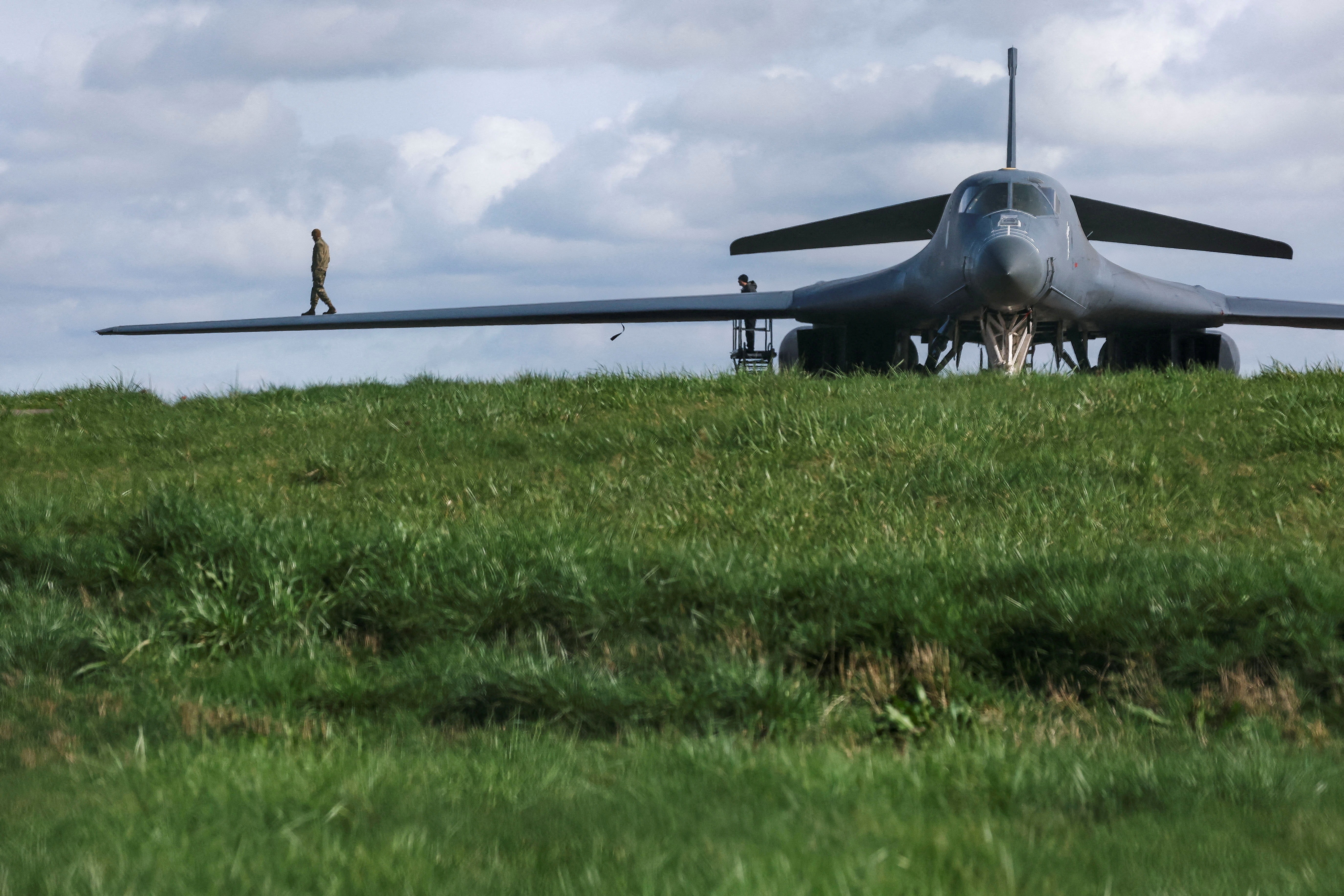 A person in uniform walks on the wing of a parked bomber aircraft.