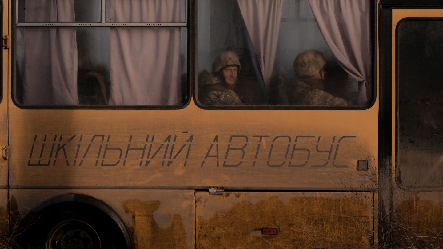 Two soldiers look out the window of a school bus.