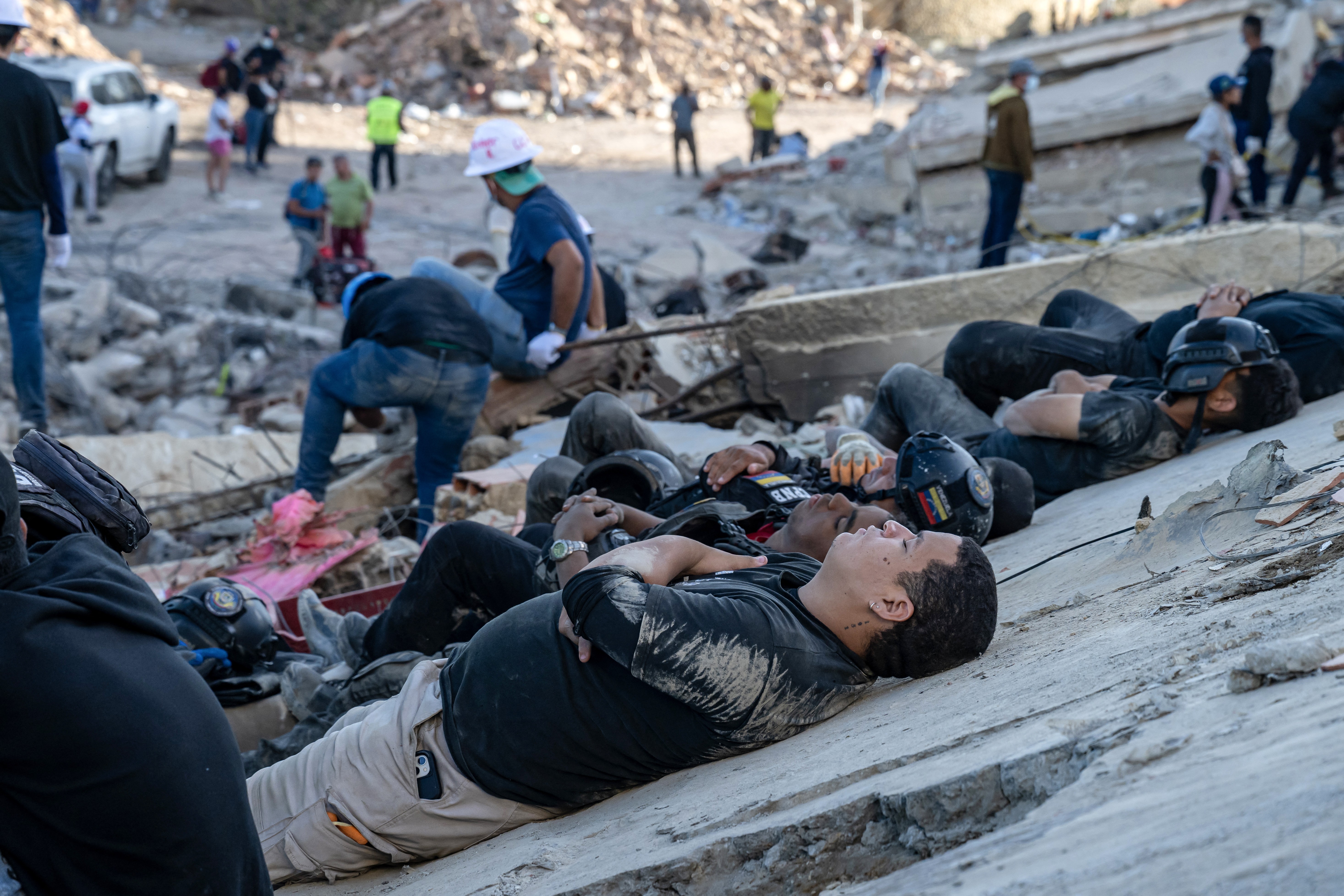 Exhausted rescuers and volunteers rest on the rubble of collapsed buildings.