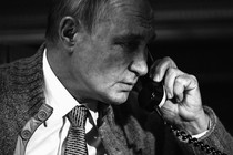 A black-and-white photo of Vladimir Putin holding a phone to his left ear