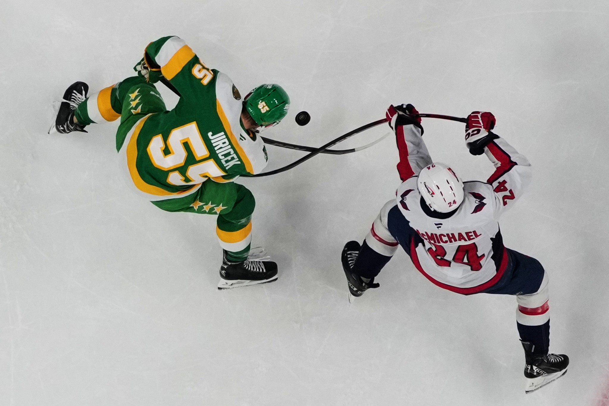 Two hockey players cross sticks, vying for a puck.