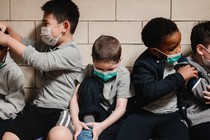 A group of young kids in face masks sit on a bench.