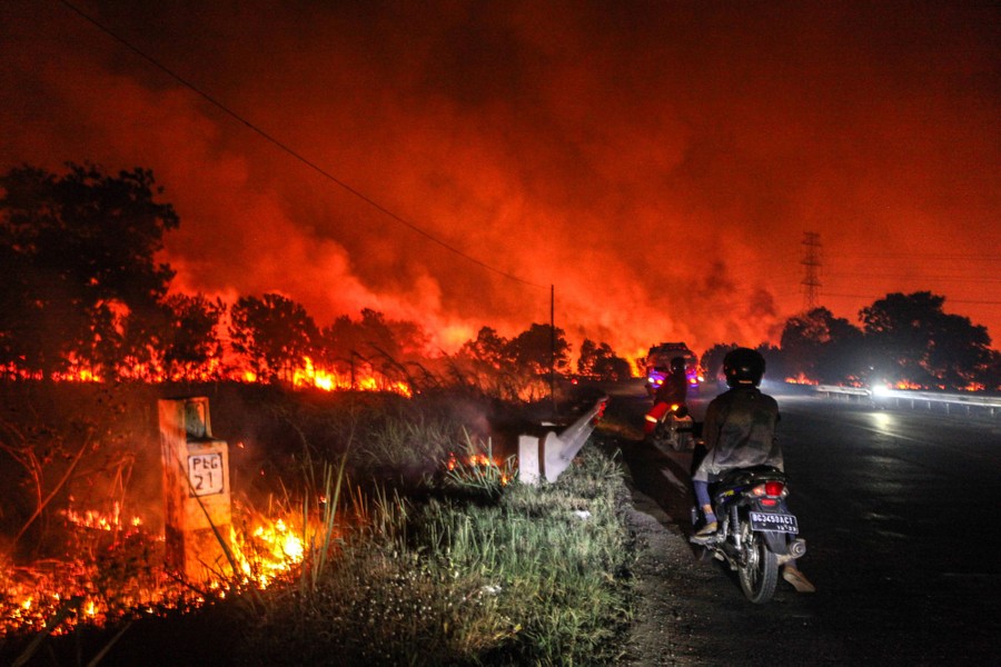 Several cars stop on a road at night, with smoke and fire rising all around nearby.