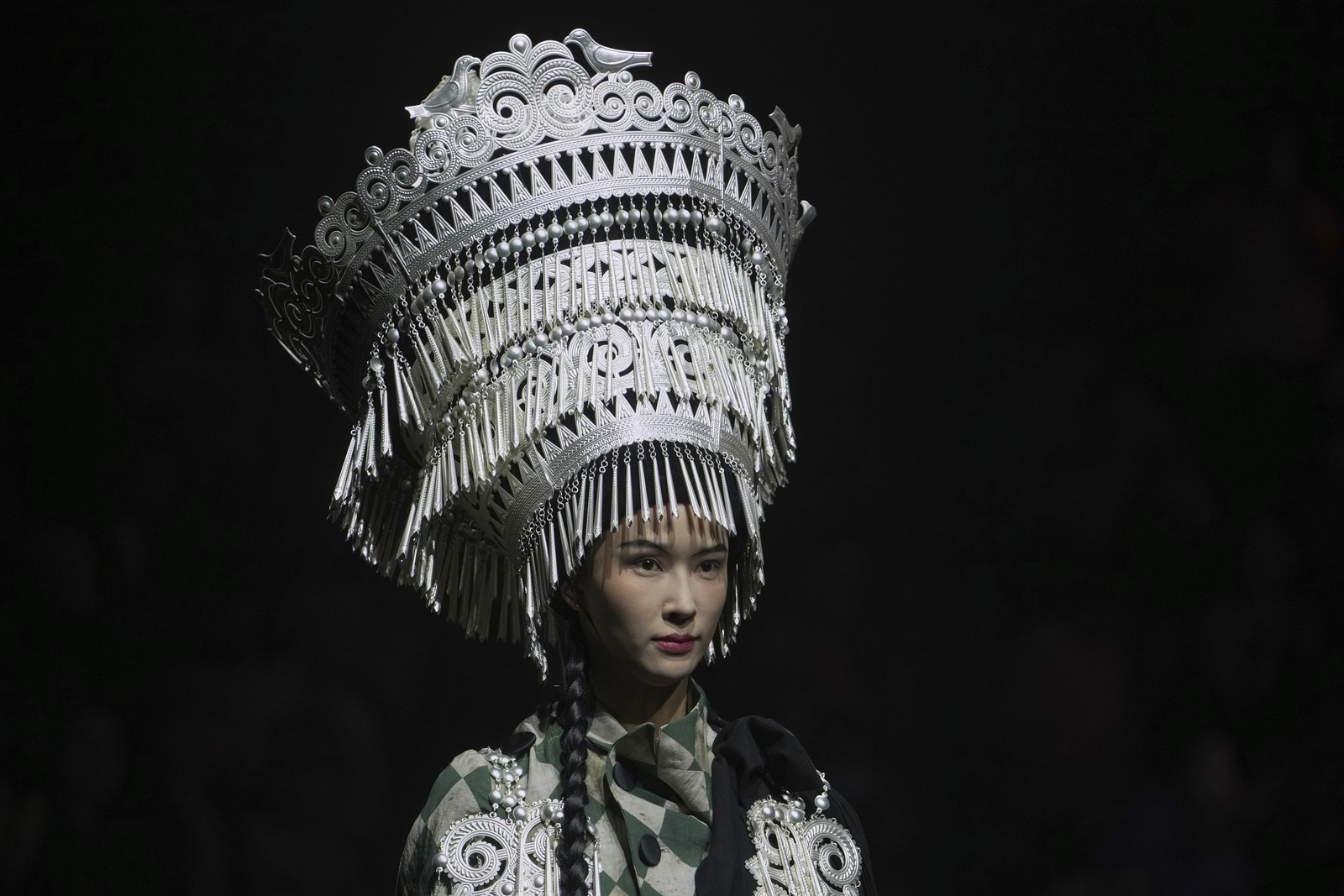 A model walks on a runway, wearing a large traditional headpiece.