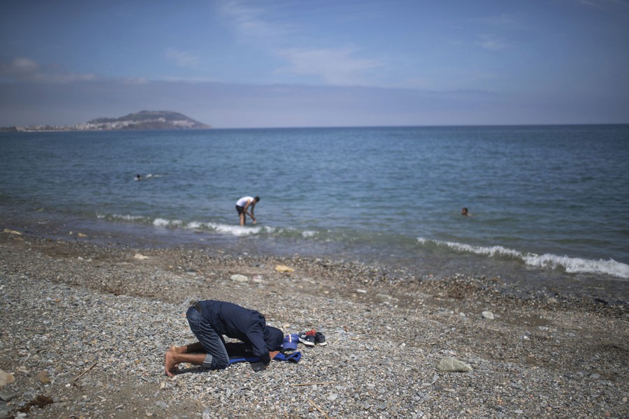 A boy kneels in prayer on a beach.