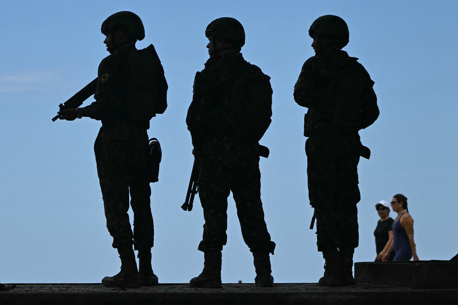 Three soldiers are seen in silhouette against a blue sky.