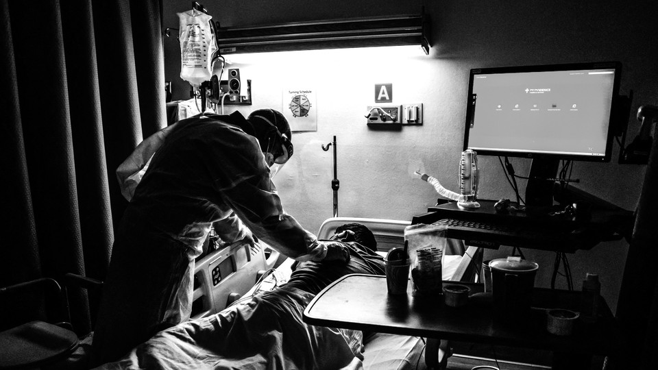 A nurse takes care of a COVID patient who is lying on his stomach in a hospital bed.