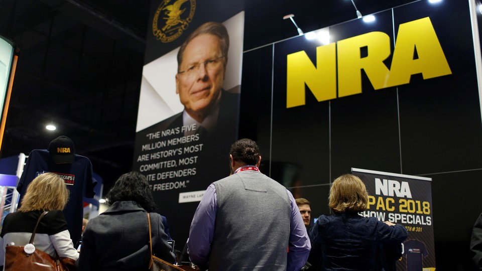 People in front of a booth with a picture of Wayne LaPierre and the NRA logo