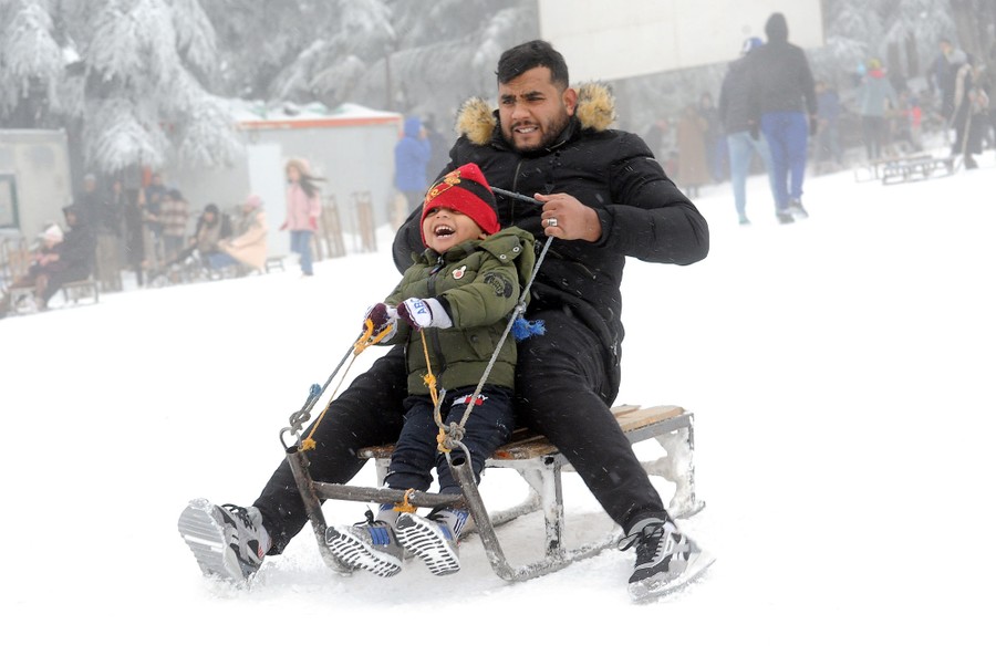 A young child smiles, riding on a sled with a man.