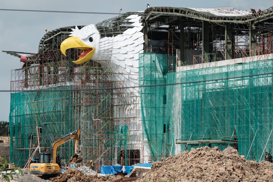A multistory building, under construction, faced with a large sculpture of a bird of prey