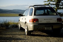 A white Subaru parked facing a body of water and mountains.