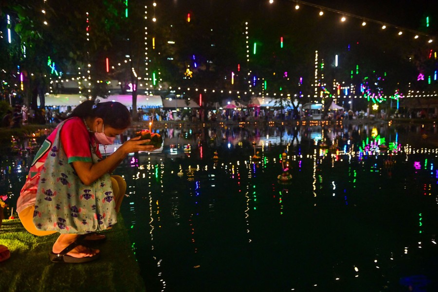A woman sets a small decorative raft into a body of water.