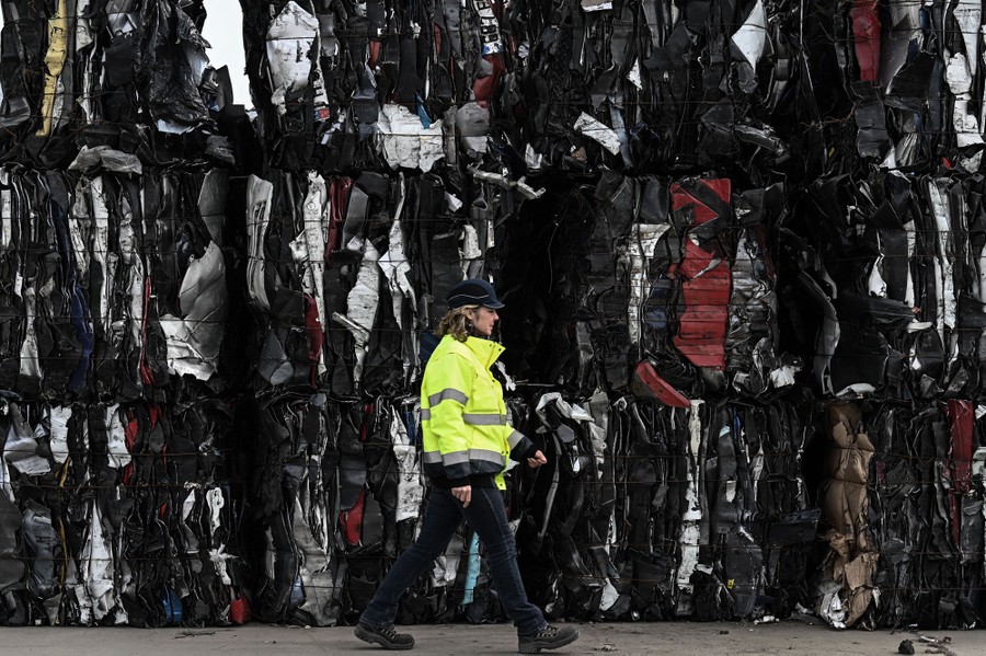 An employee walks past tall stacks of compressed cardboard at a recycling center.