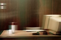 An empty desk with a boxy desktop monitor, keyboard, thermos, and coffee mug, with a stylized blur over it