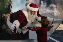 Santa Claus, entrapped in a giant snow globe, reaches out his hands towards a little boy, who also has his arms outstretched.