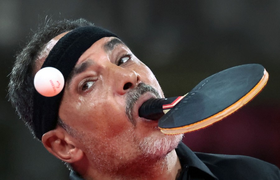A man competes in a table-tennis match holding a paddle in his mouth.