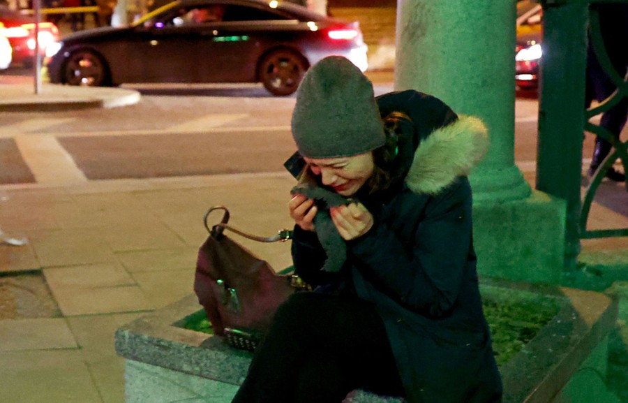A person cries while sitting on a planter on a city sidewalk.