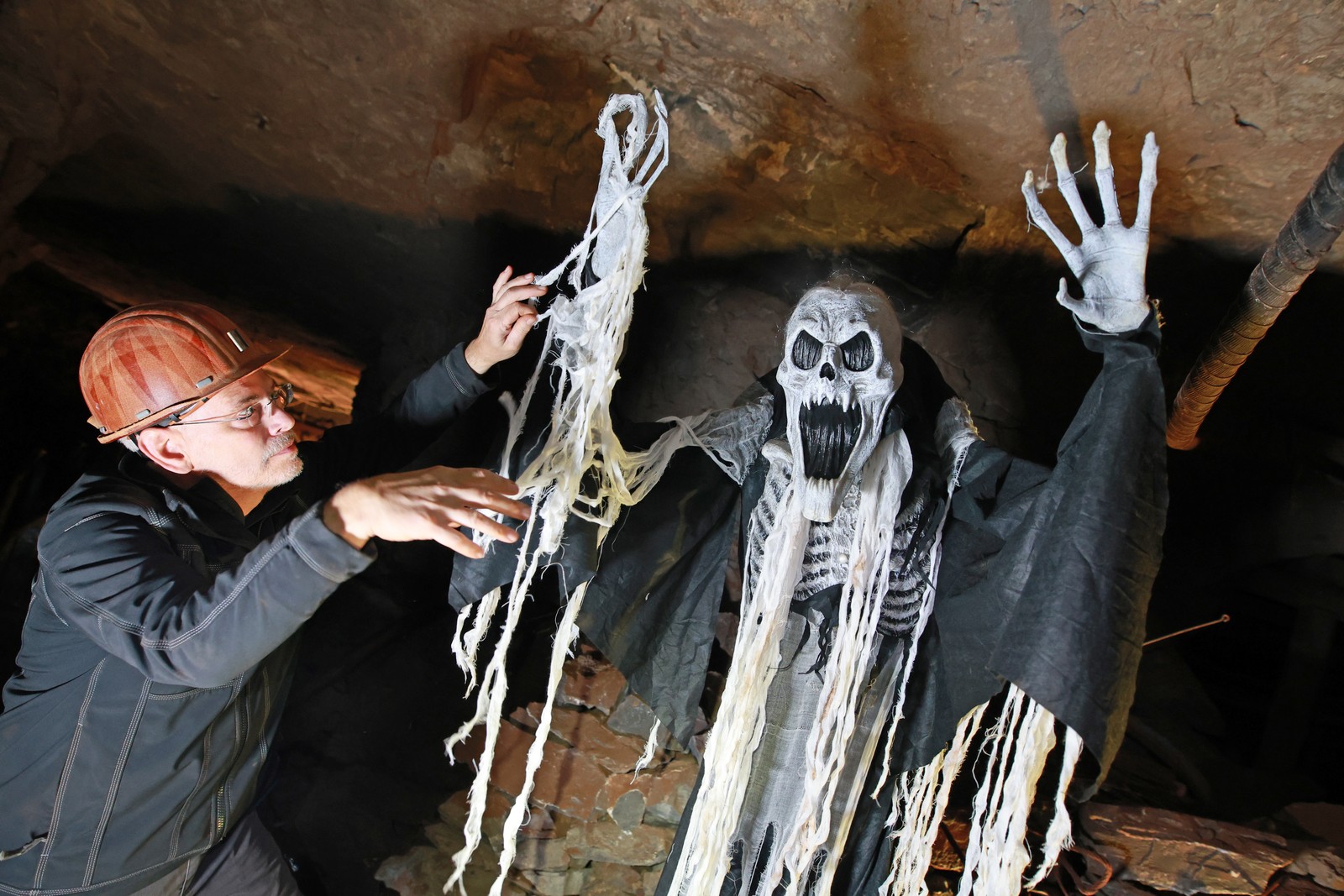 A person works to set up a life-sized scary creature statue inside a mine set up for tourism.