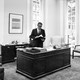 Henry Kissinger standing at a desk in an office with high windows in 1970