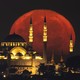 The full moon rises behind a large mosque.