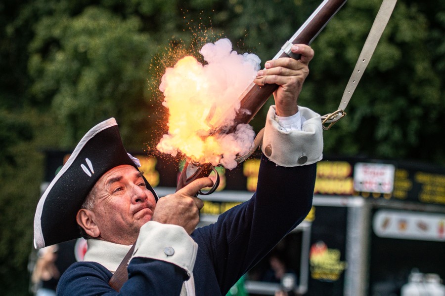 A person wearing an 18th-century costume fires an old-fashioned musket during a parade.