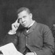 Black-and-white photograph of Booker T. Washington sitting at a desk, holding a paper