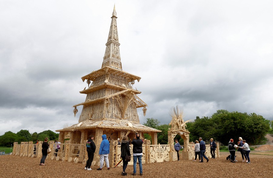 Several people stand outside a tall wooden pyramidal structure.