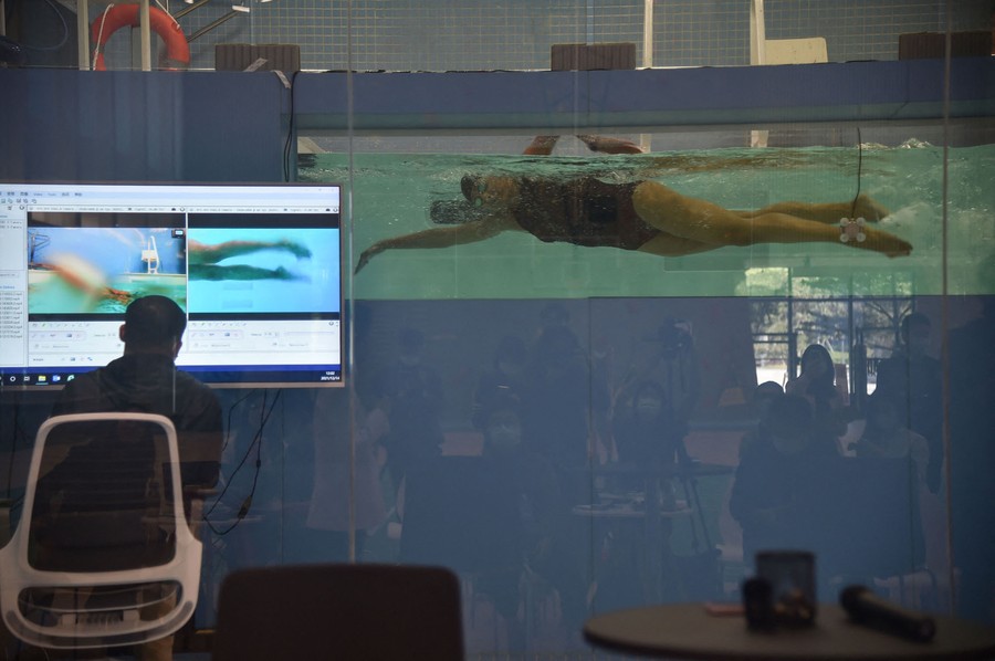 A person swims in a pool while being watched on a screen by a technician.
