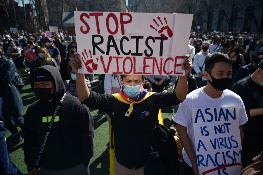 Hundreds of people take part in a protest. One protester in front holds a sign saying "Stop Racist Violence."