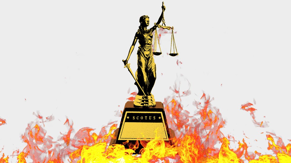 A statue of lady justice is surrounded by flames.