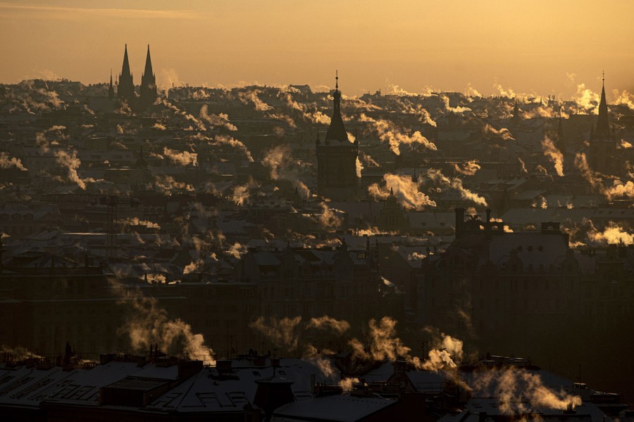 Smoke rises from many chimneys seen in a broad view of Prague.