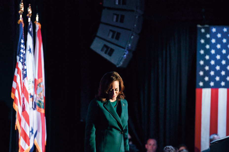 photo of Kamala Harris in spotlight on stage with flags in background