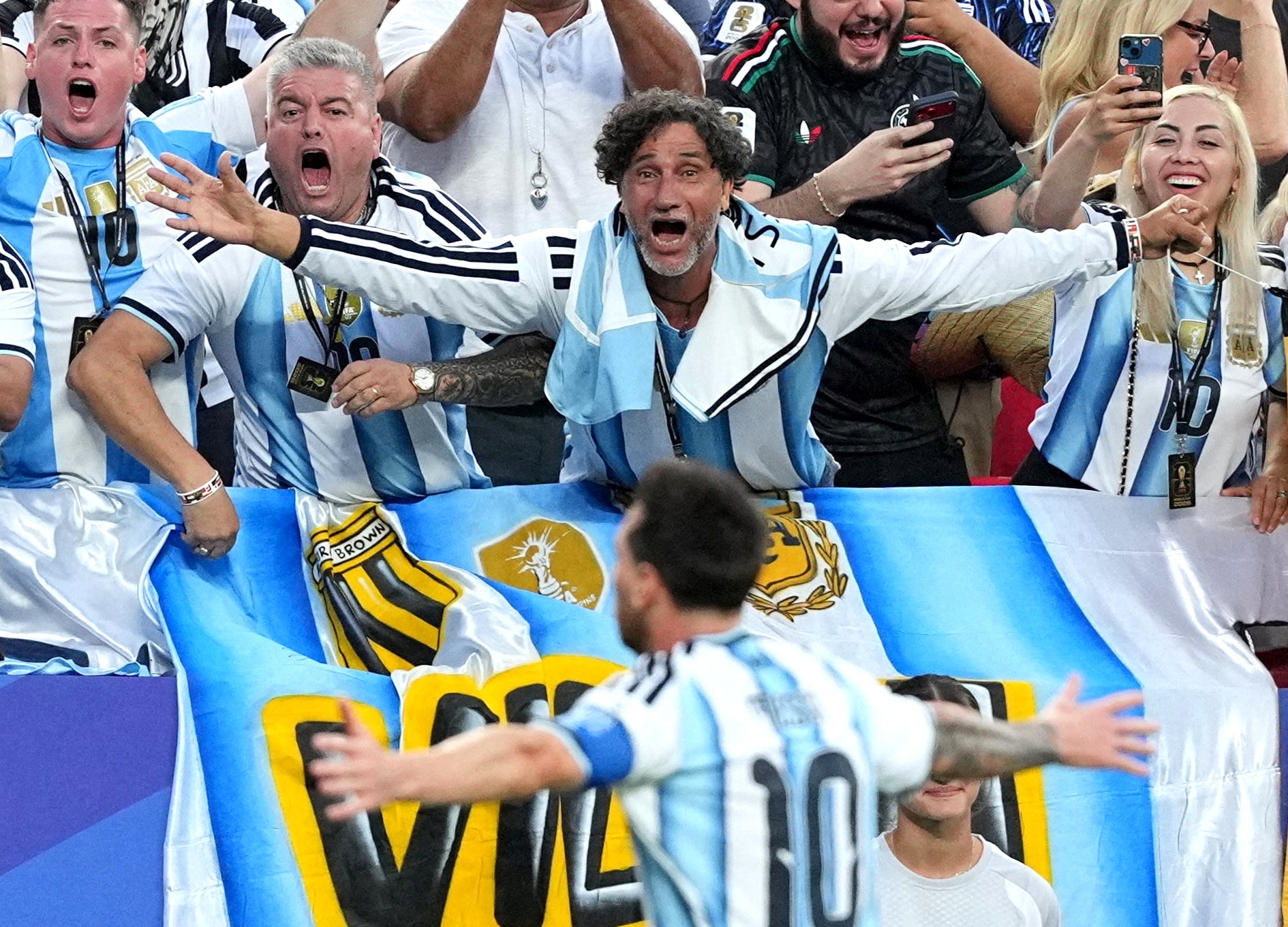 Fans in a stadium cheer with Argentina’s Lionel Messi as he runs past, celebrating scoring a goal.