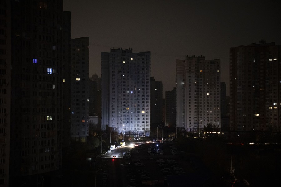 A night view of city buildings, mostly dark, with a small scattering of windows showing light.