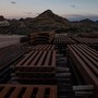 Stacks of steel bollards sit in a desert. In the background, a blasted mountain and Donald Trump's unfinished wall.